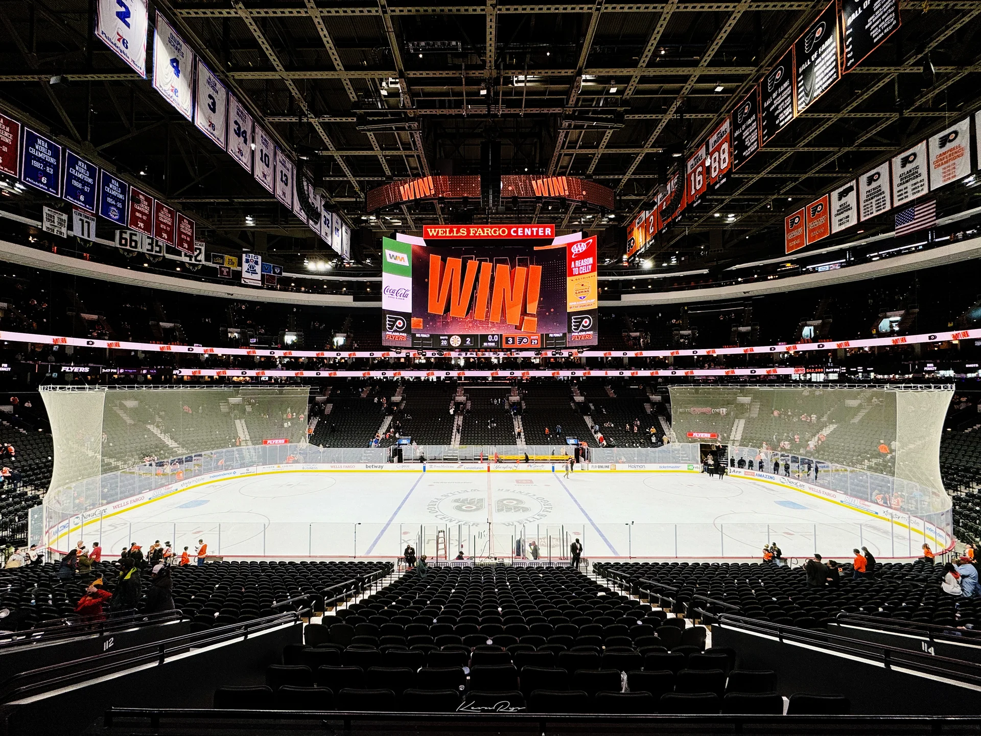 An empty lower bowl looks out on the ice, with the scoreboard reading WIN! under banners hanging from the rafters