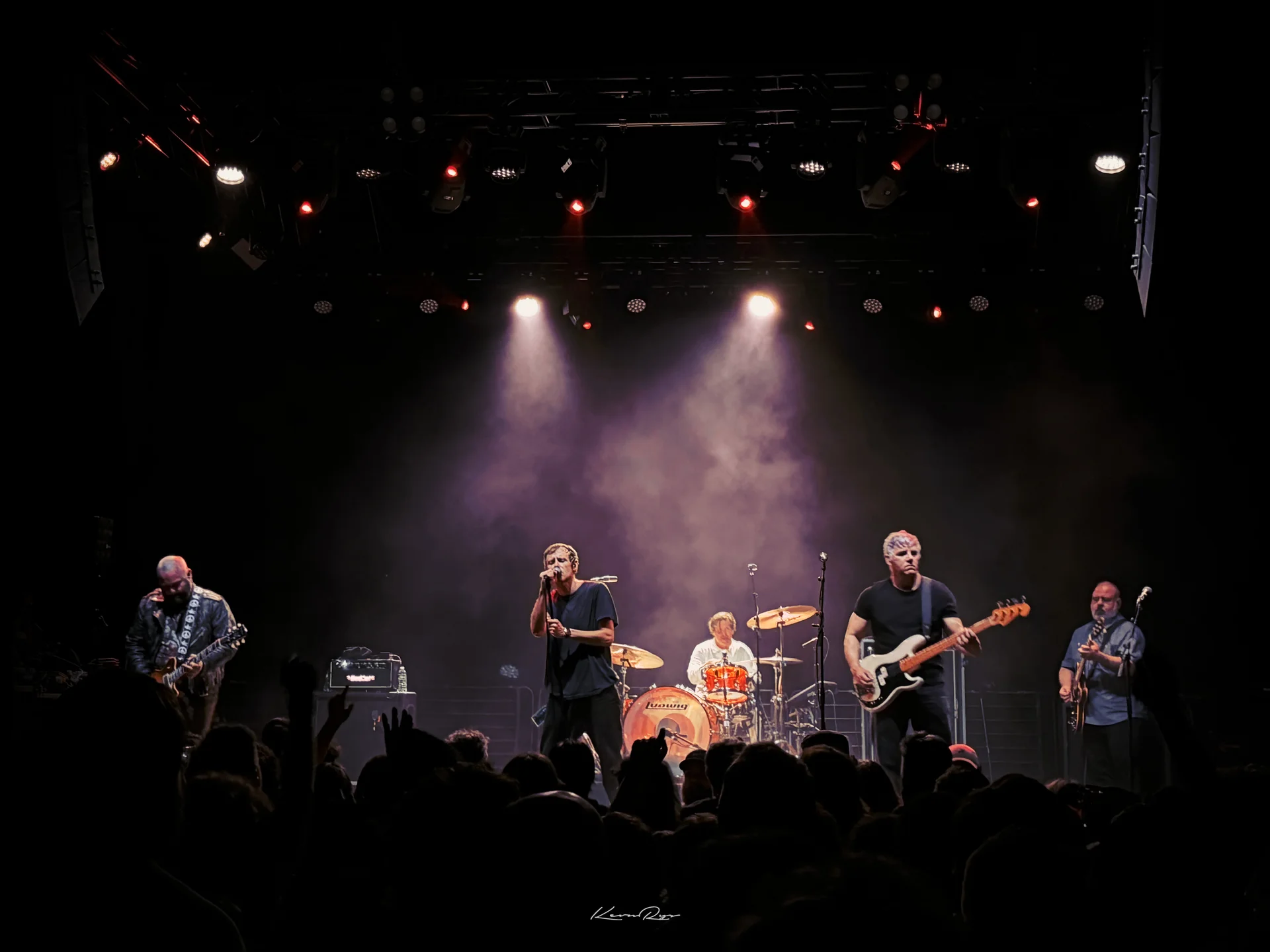 A five-piece band plays under purple haze, spotlights beaming from the rig above, the crowd silhouetted in front